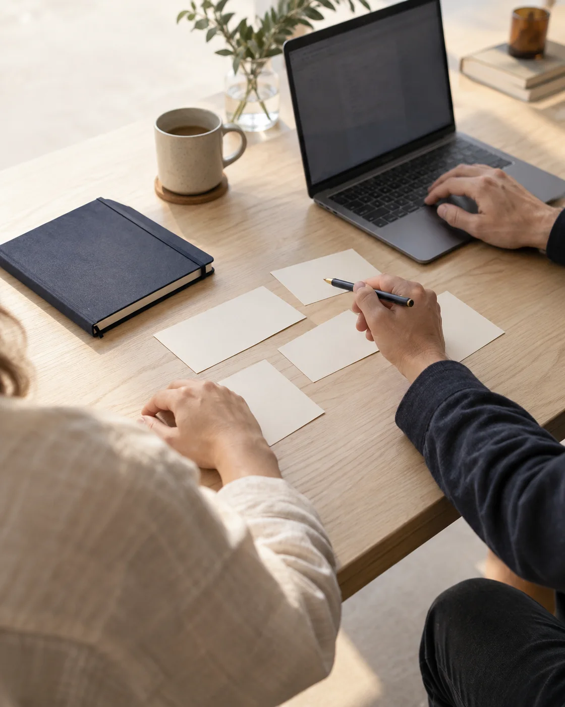 Hands mapping a workflow together at a light oak desk.